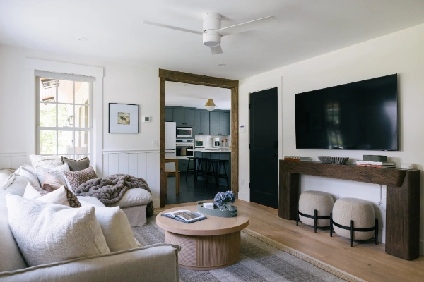 Living room perspective showing media console, wall-mounted television, wide doorway into kitchen, and layered neutral decor